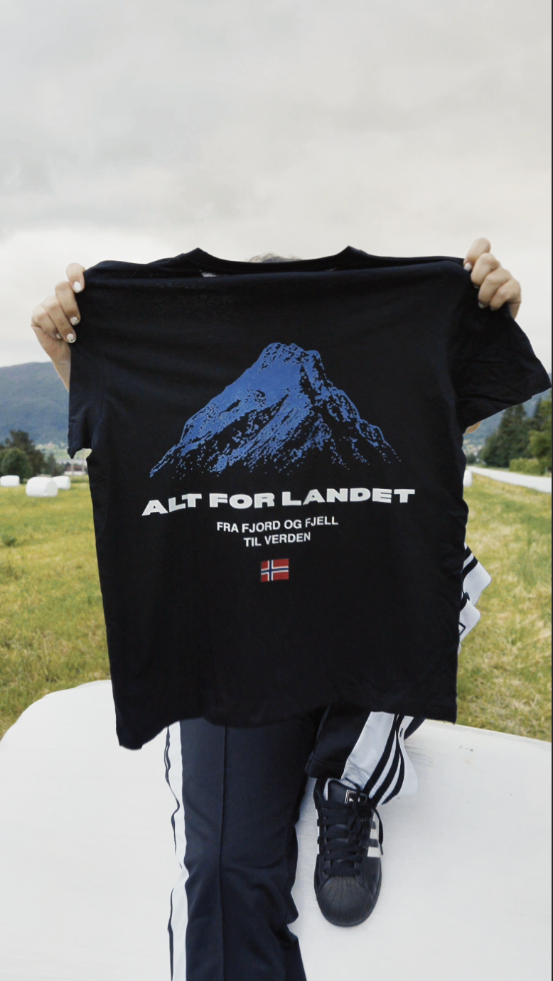 Holding up the Alt for Landet tee in a field